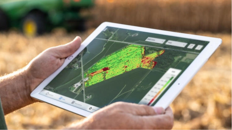 A close-up shot of a person in a crop field holding a tablet that is displaying a data map